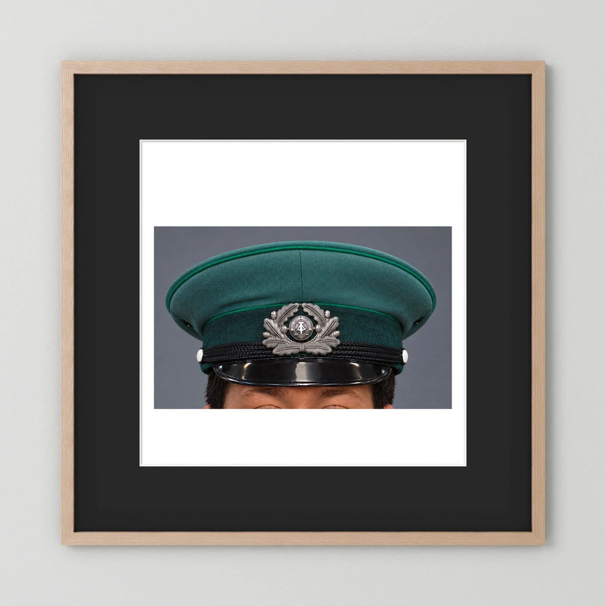 East German Volkpolizei (People's Police), Visor Cap, January 1989 — photograph displayed in a natural oak frame mockup
