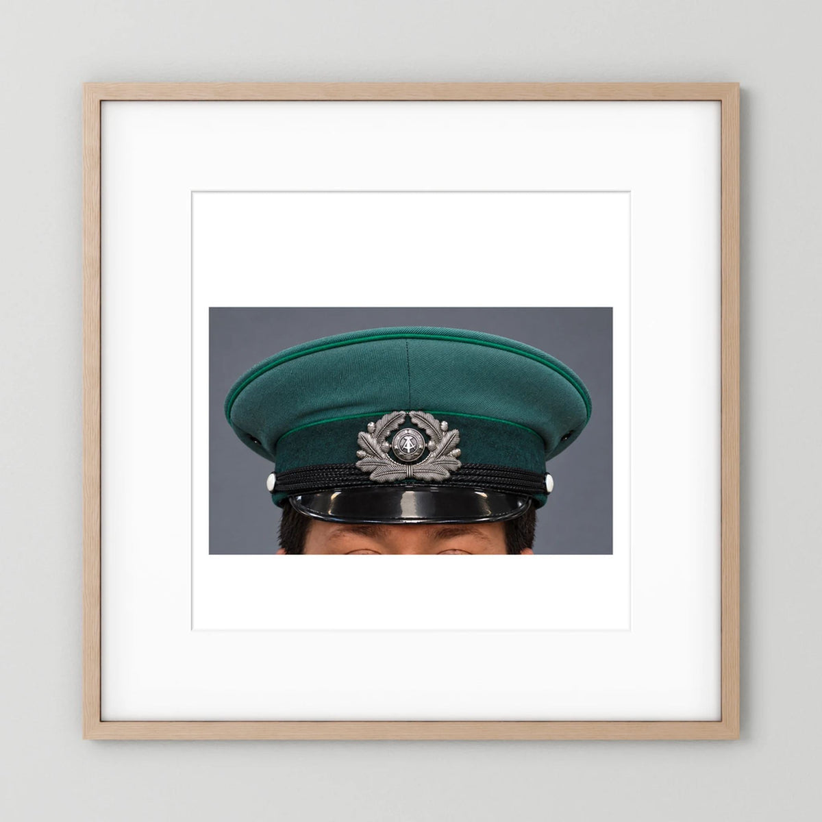 East German Volkpolizei (People's Police), Visor Cap, January 1989 — photograph displayed in a natural oak frame mockup